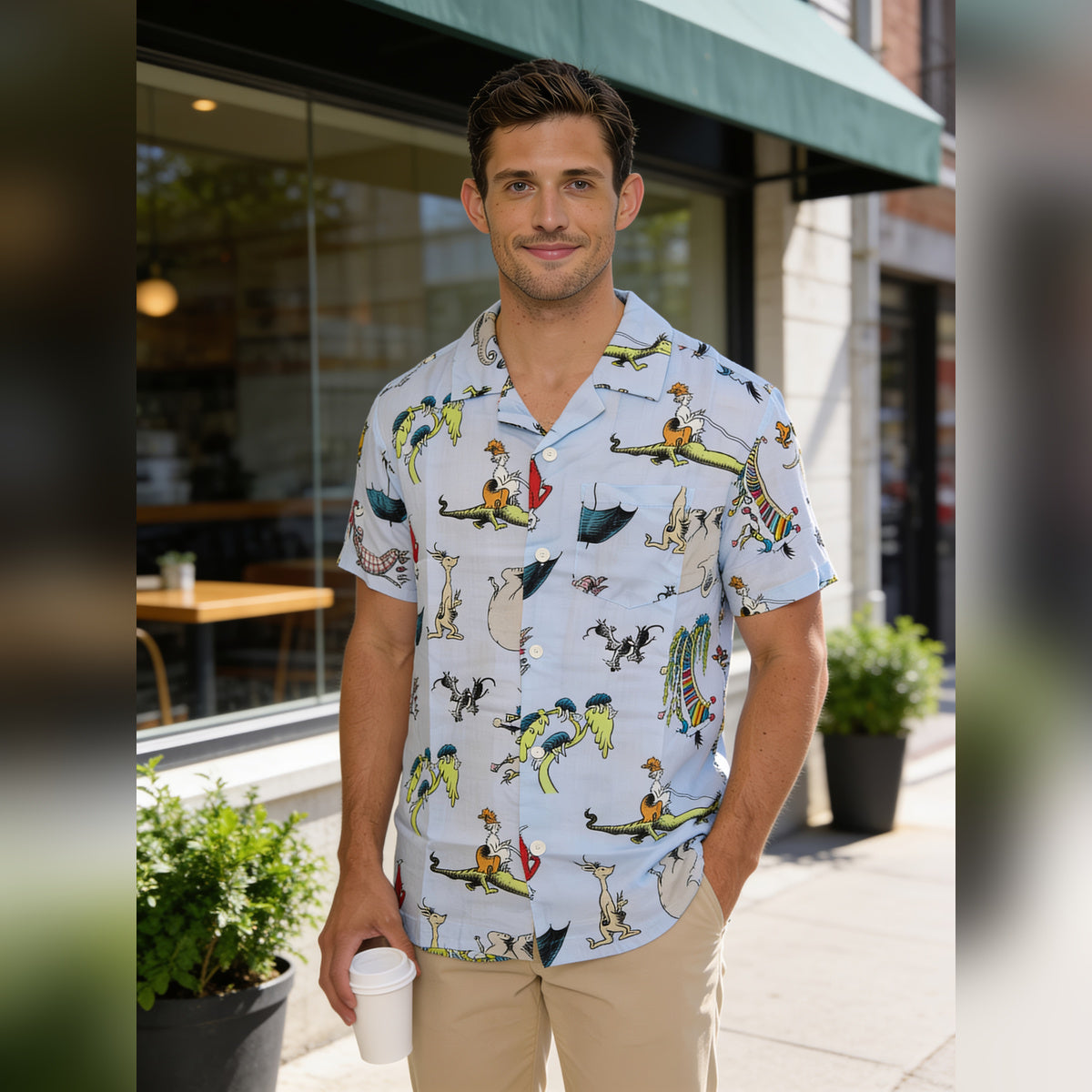Man holding a coffee outside a cafe in the light blue Dr. Seuss button up shirt