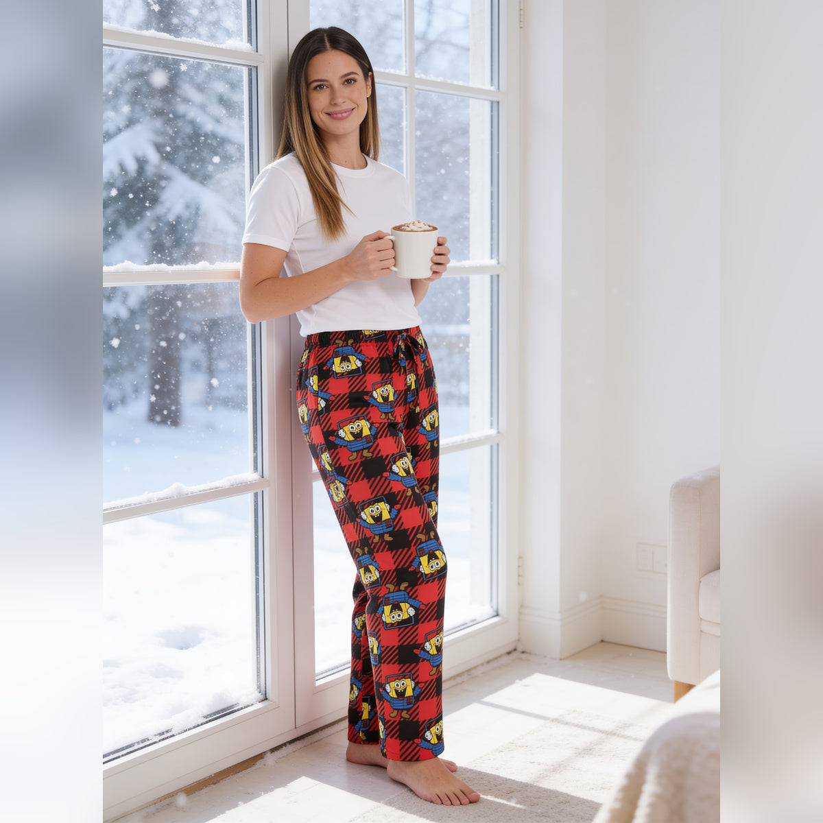 Woman holding a mug by a snowy window in the SpongeBob Puffer and Snow pants
