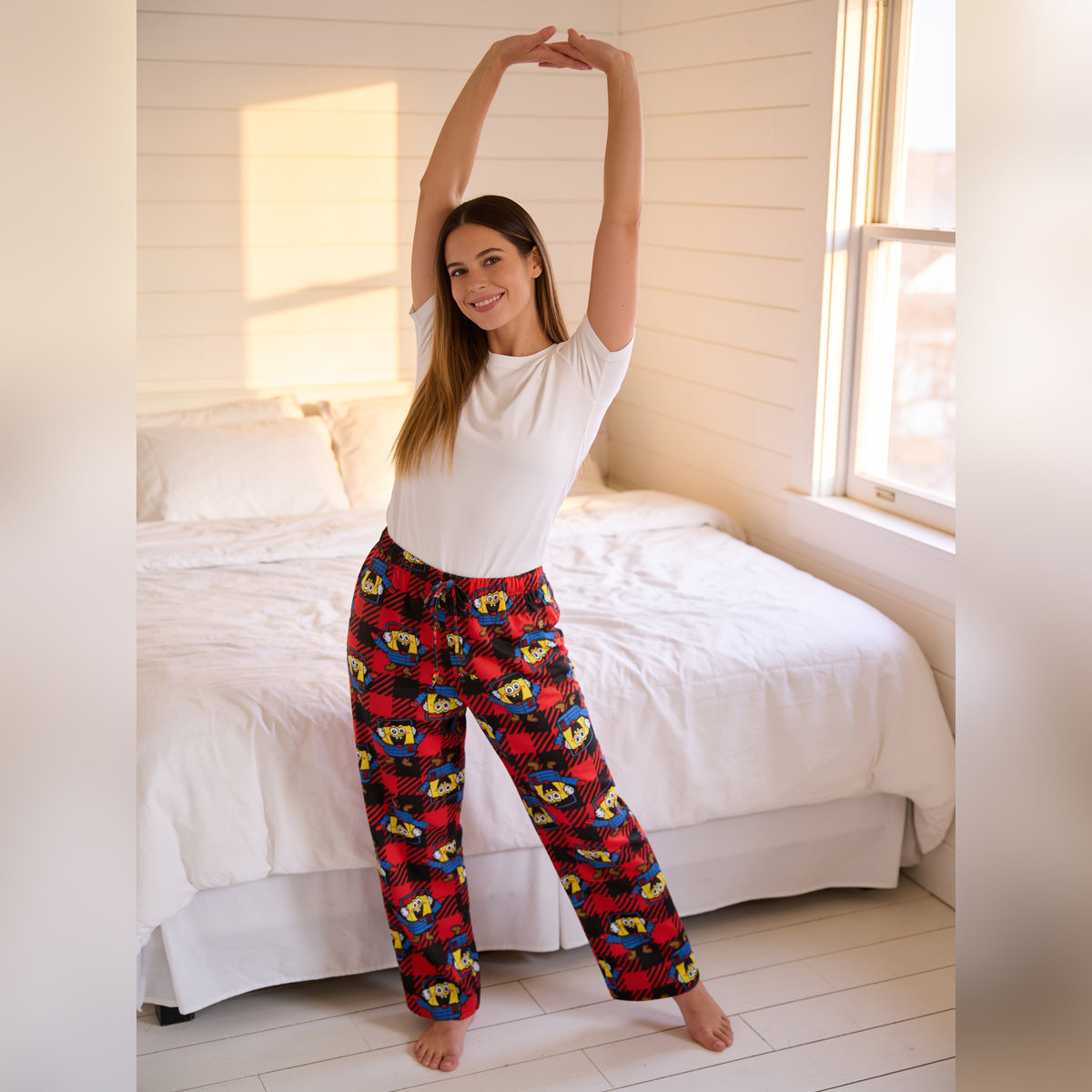 Woman stretching in a bedroom wearing the SpongeBob red plaid sleep pants