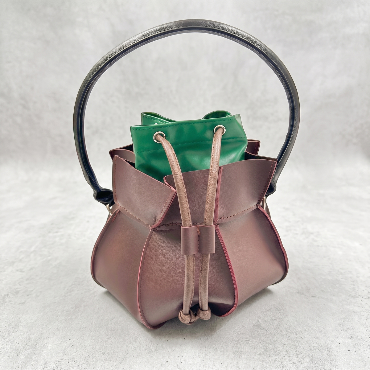 Brown leather cauldron purse with drawstring and green lining on a light grey textured background